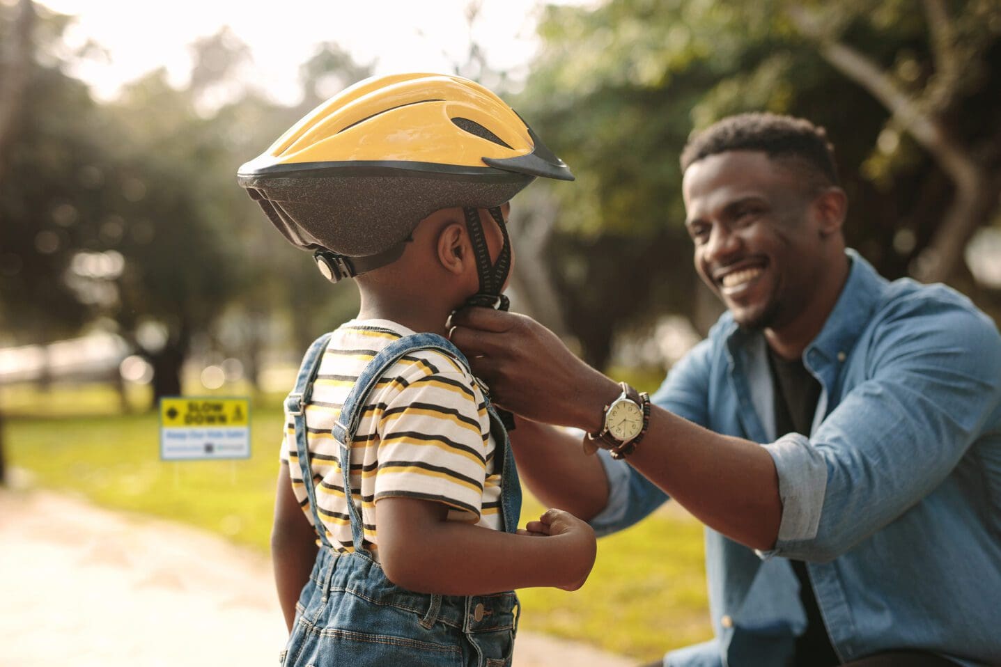 fastens protective helmet for learning to ride bicycle at park. Father helping his son to wear a cycling helmet.