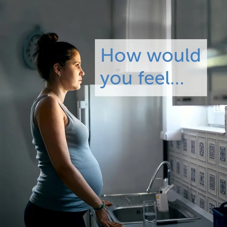 Sad-looking pregnant woman staring out of her kitchen window